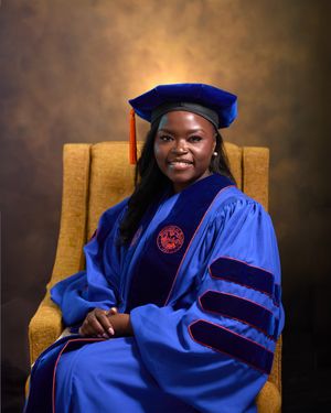 Formal graduation portrait in doctoral regalia seated in gold chair.
