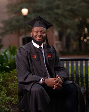 Graduate in black cap and gown seated on bench during evening graduation photoshoot.