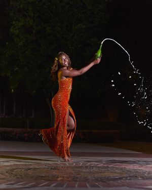 A person in a sparkly orange dress splashes water from a bottle in a dramatic nighttime photo shoot.