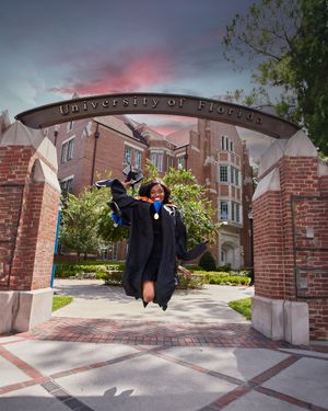 Graduate celebrates under University of Florida arch during dramatic sunset.