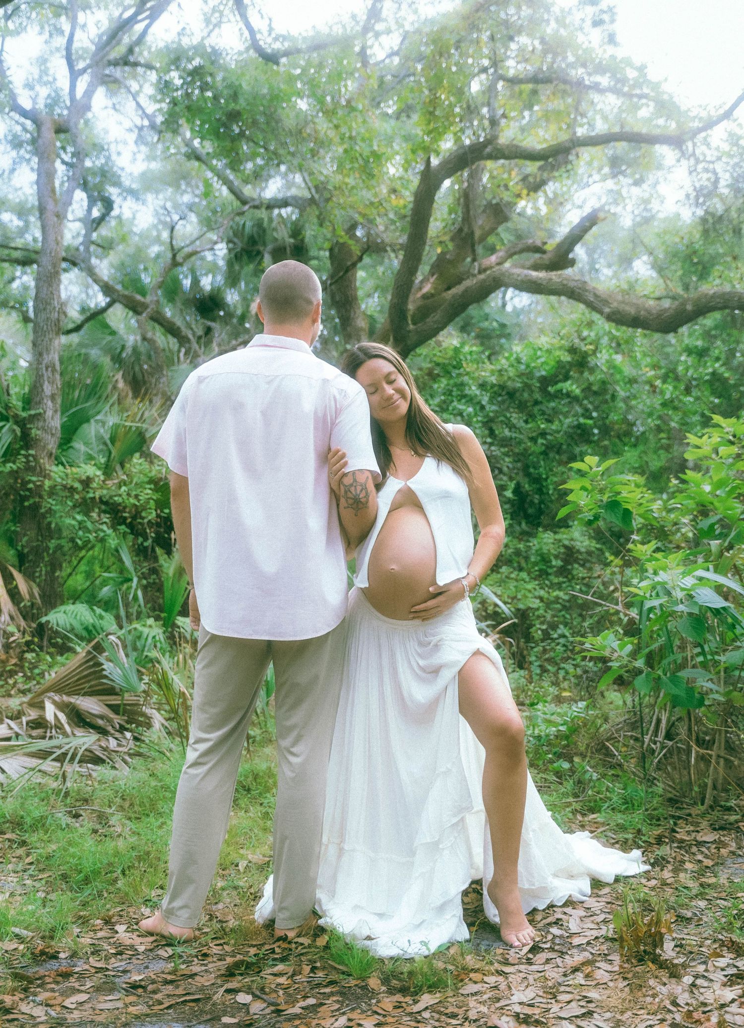 A couple poses together in a dreamy garden setting surrounded by lush greenery and winding tree branches.