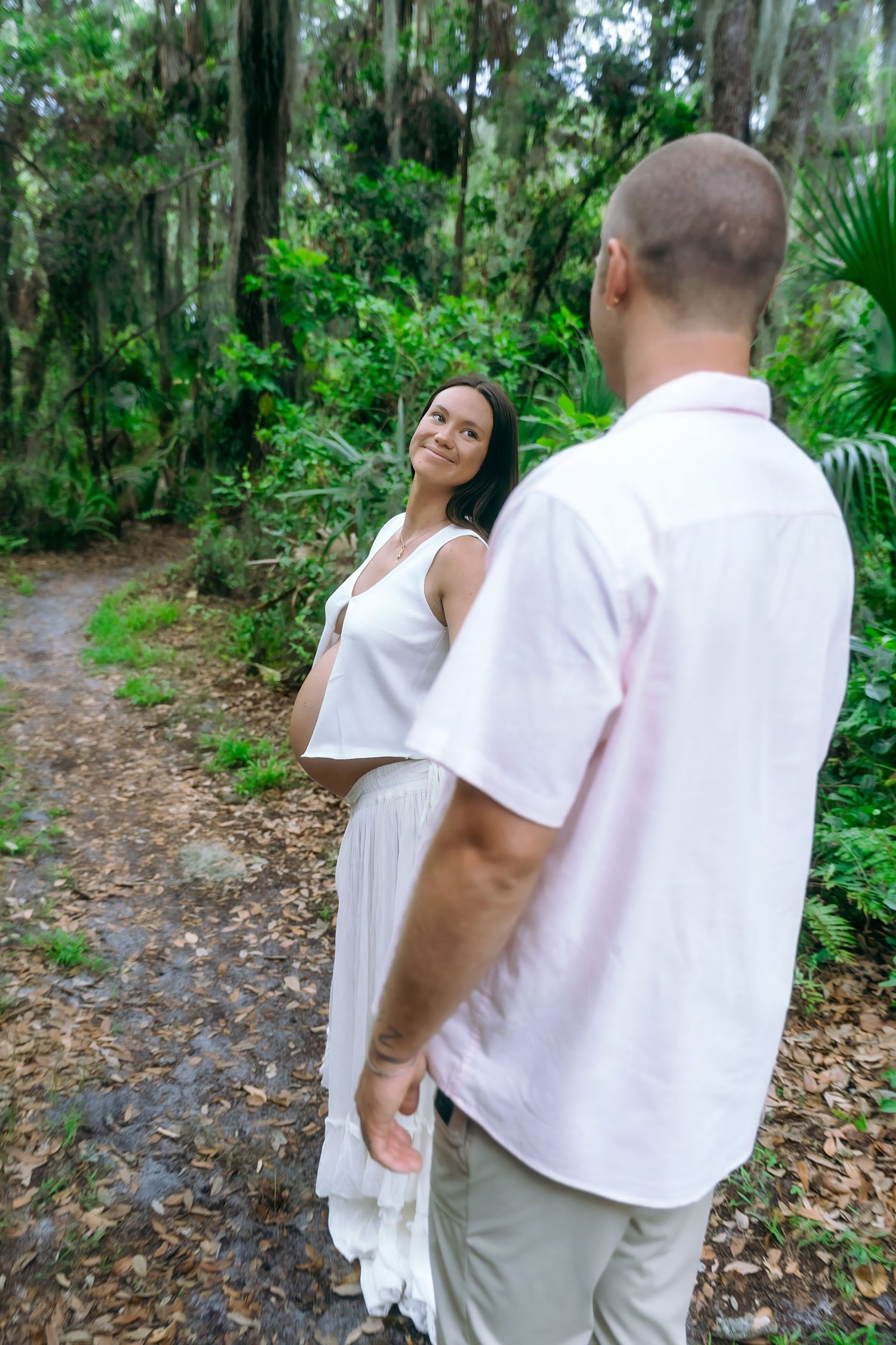 A couple in white attire sharing romantic moments on a forest trail surrounded by lush tropical vegetation.