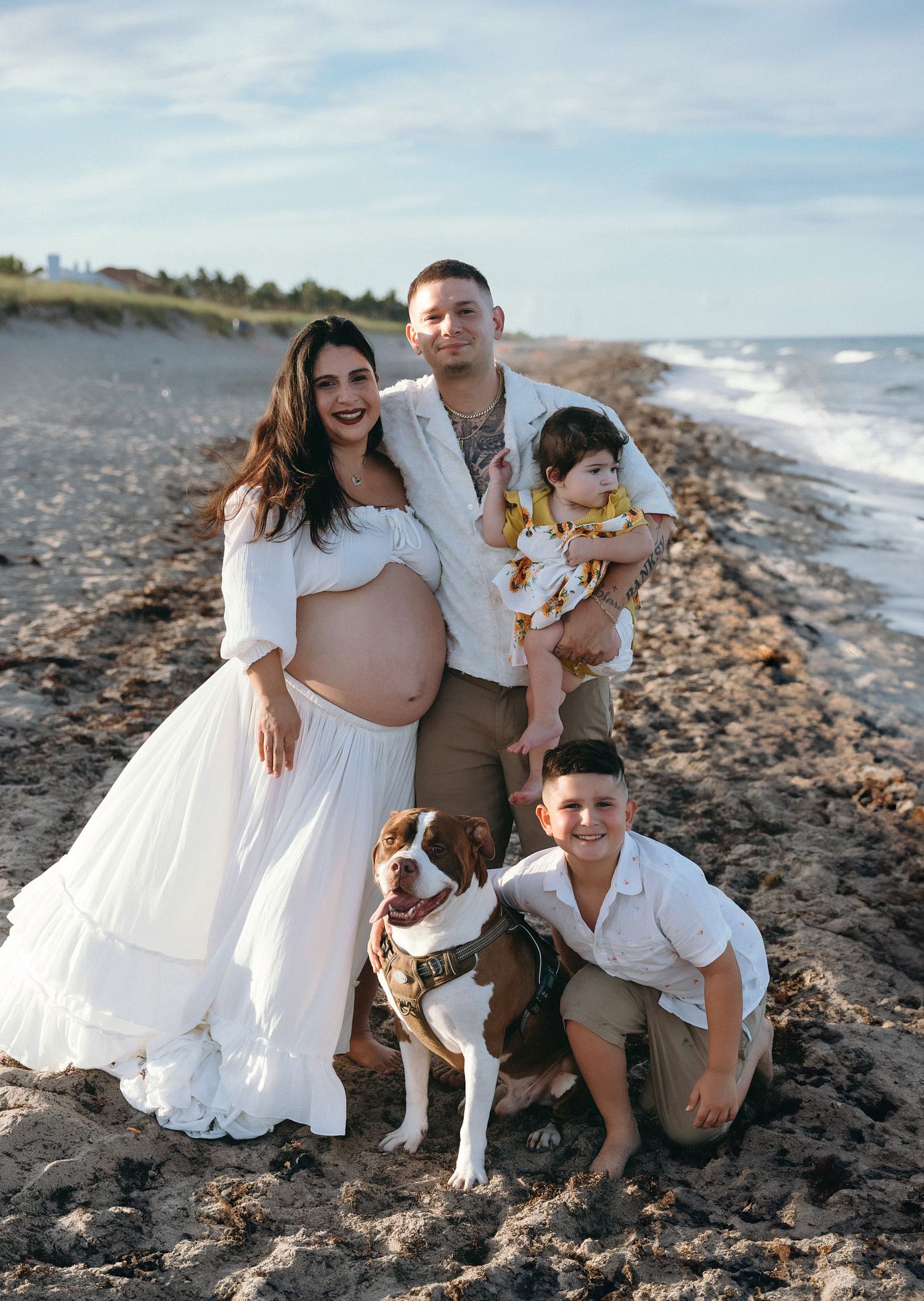 Family dressed in white sits together on a rocky beach along the ocean shore during a photoshoot session.