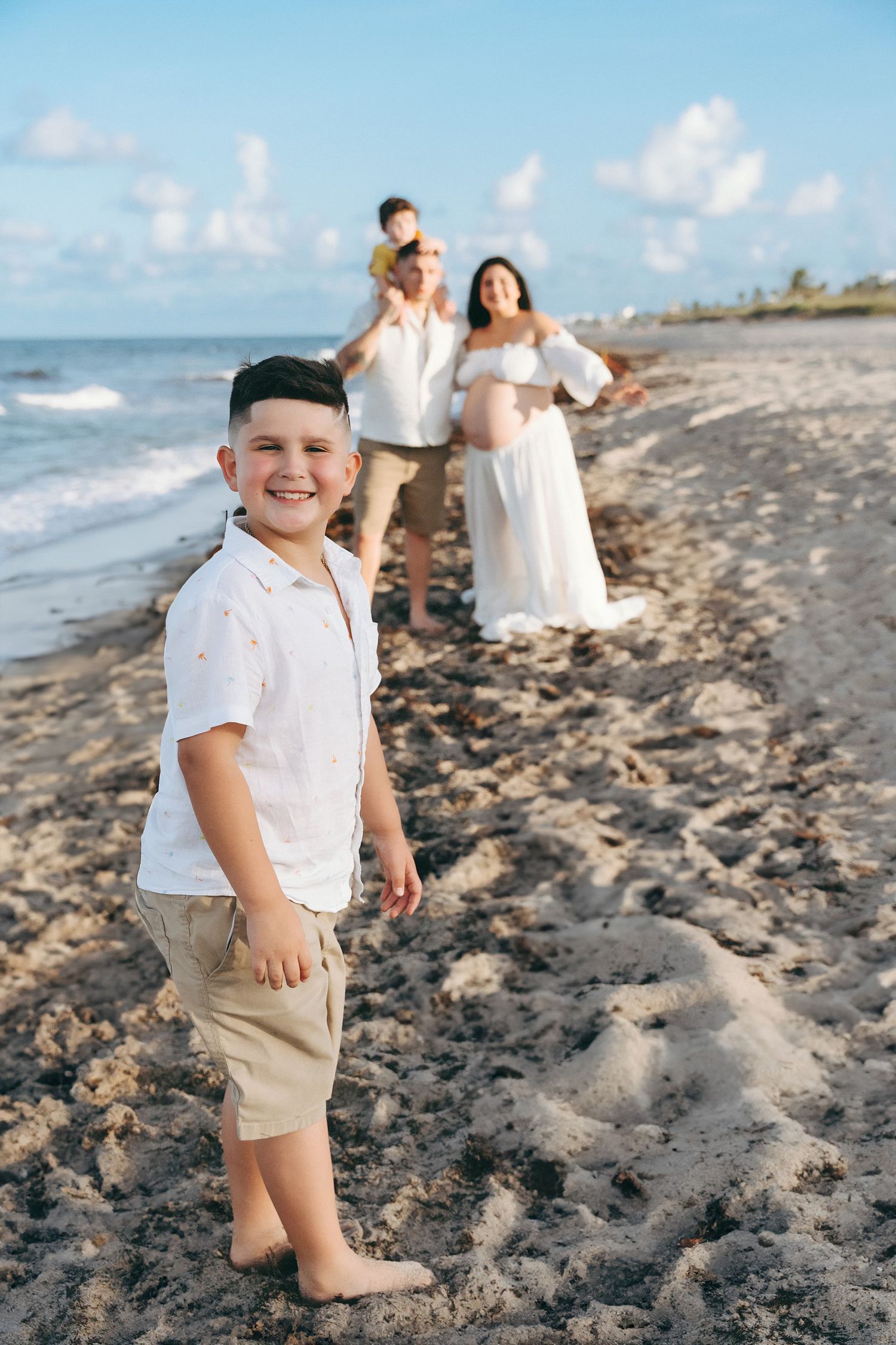 A family enjoys a sunny day together on a beach with waves and sand, creating precious memories by the ocean.