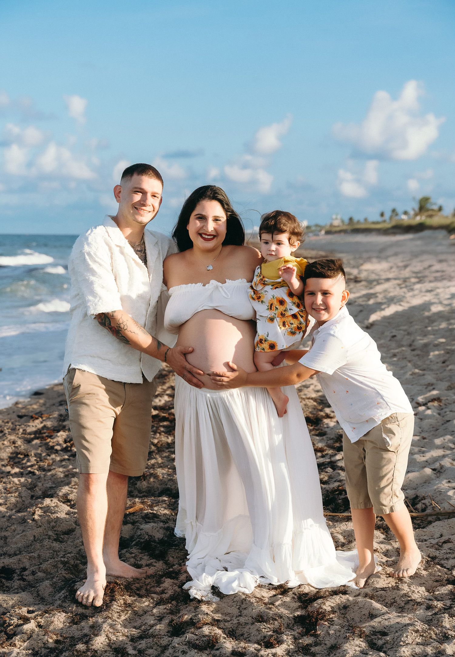 A family poses together on a beach during sunset with waves and palm trees in the background.