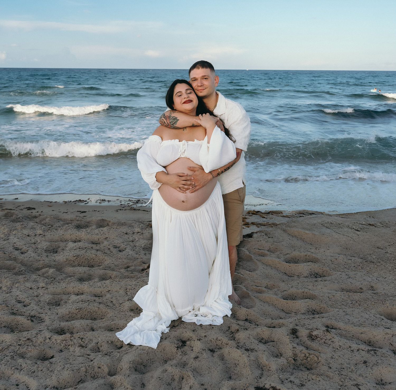 A couple shares an intimate moment on the beach at sunset with waves crashing behind them.