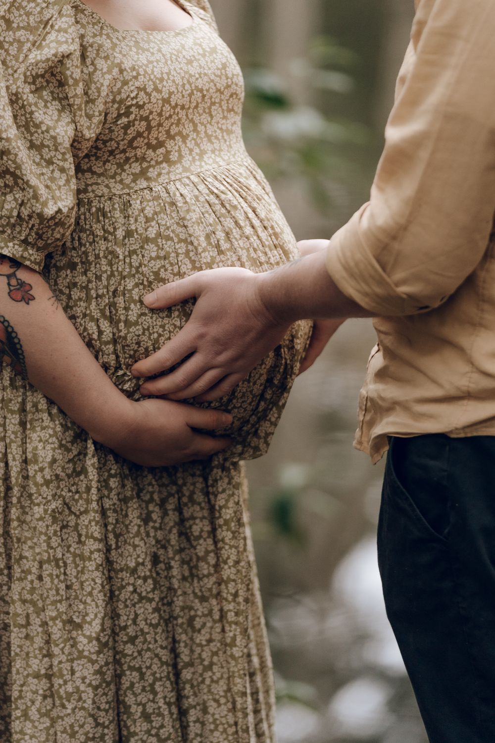 A pregnant woman in a floral dress while partner's hand rests on her belly.