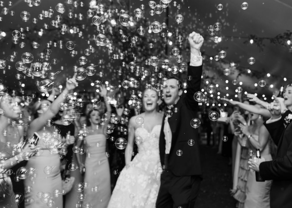 A newlywed couple celebrates under a shower of confetti and bubbles during their reception exit amidst a joyous crowd.
