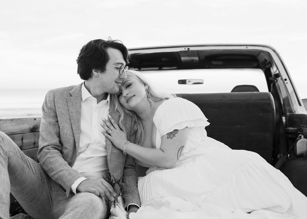 A vintage black and white photo showing a romantic couple resting together in the back of a vehicle.