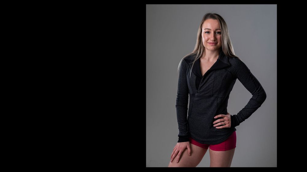 Studio portrait against grey background featuring black button-up shirt and red shorts.
