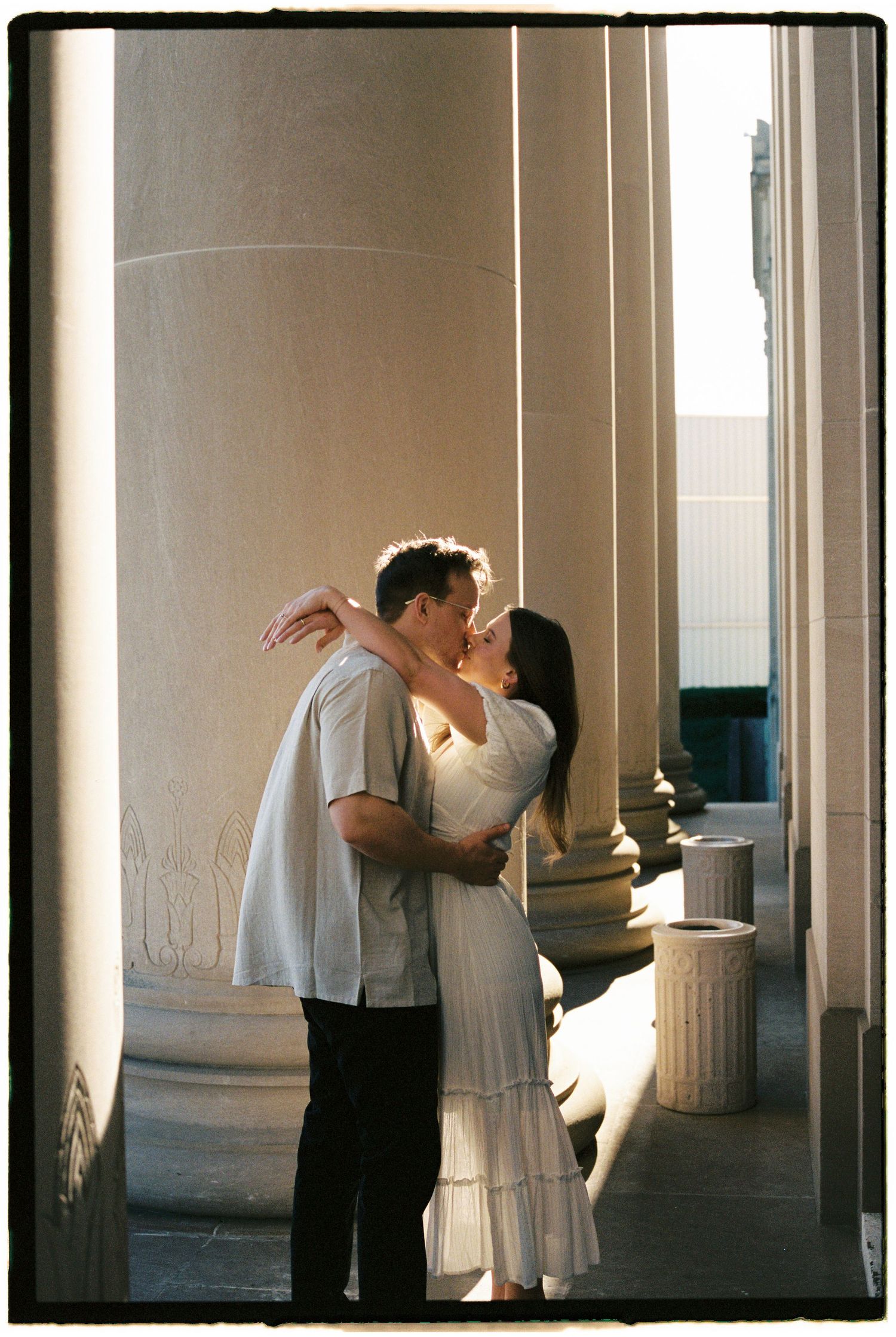 A romantic couple in white clothing embraces in a sunlit colonnade in front of the Nelson Atkins Museaum in Kansas City on film