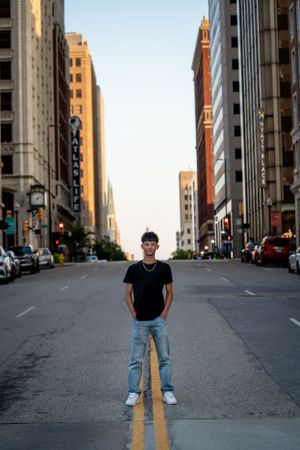 Confident teen boy in black tee standing on empty city street at golden hour downtown.