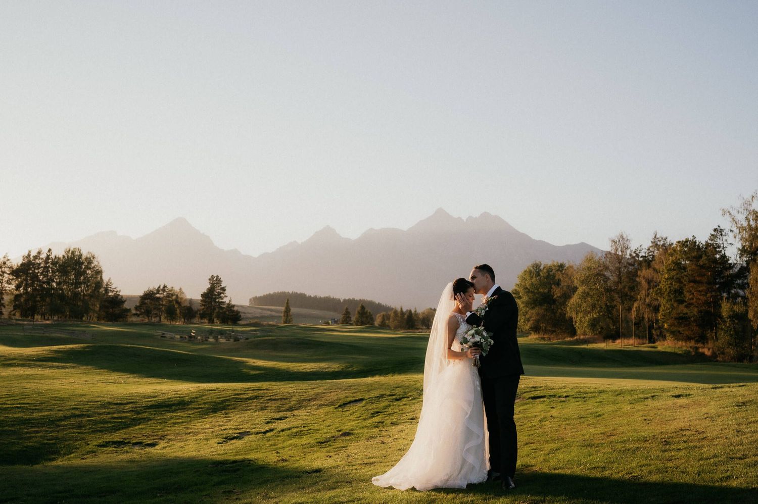 Scenic wedding portrait with couple embracing on golf course with mountain range backdrop.