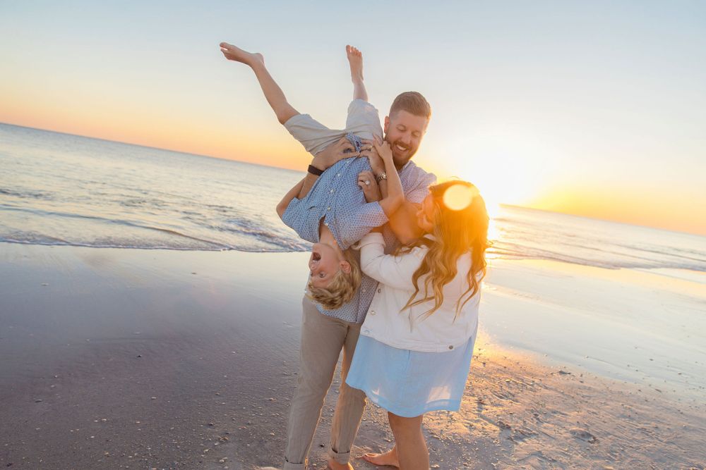 A couple shares a playful moment at sunset on the beach with the golden sun glowing on the horizon.