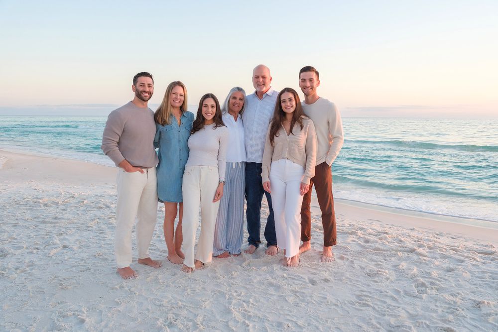 A group poses together on a white sandy beach at sunset with ocean waves in the background.