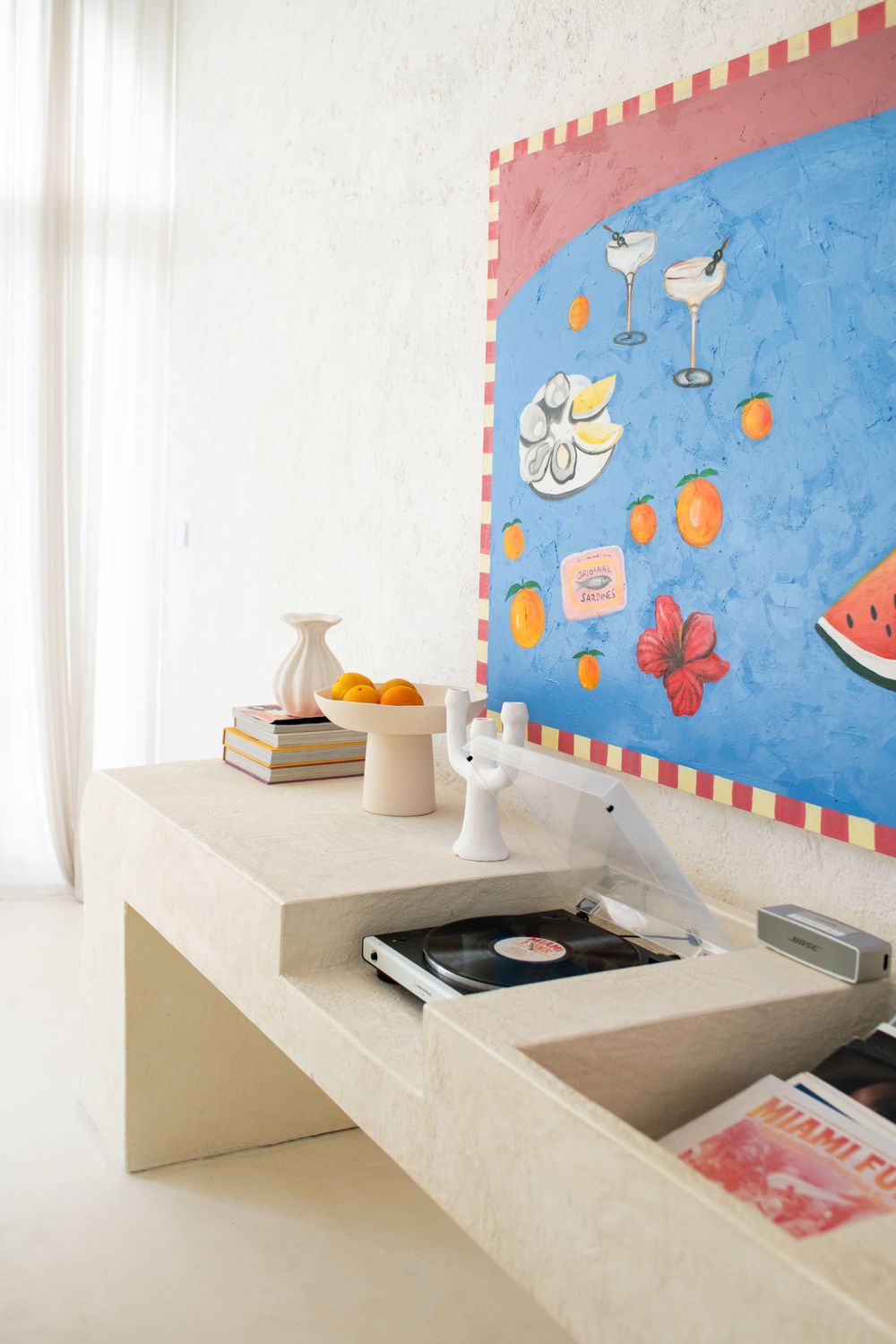 Painting on a wall on top of a table with a record player, records and decor