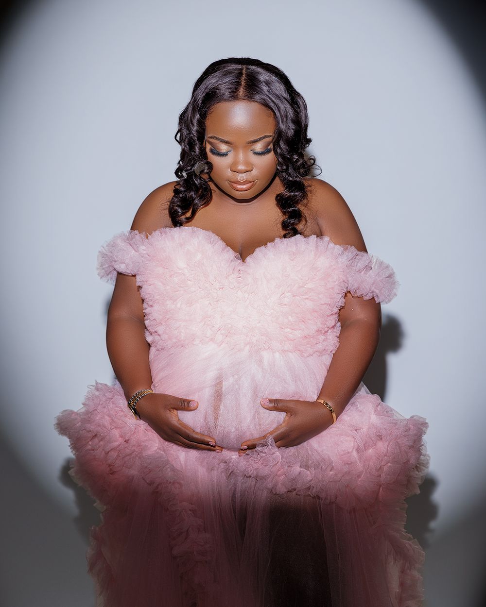 A dreamy portrait in a pink tulle gown with off-shoulder details against a gray backdrop.