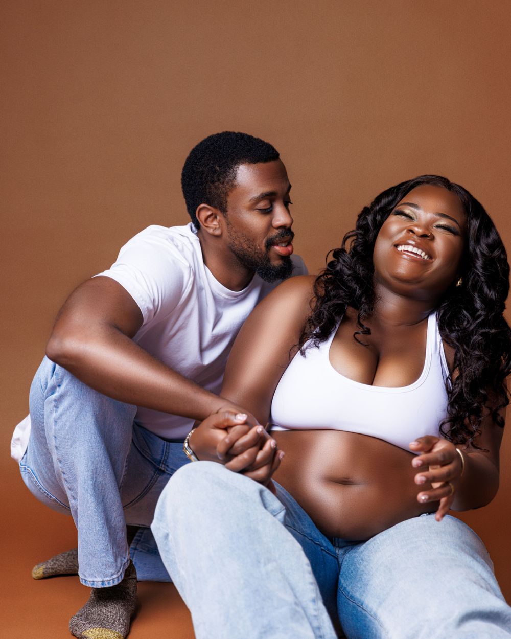 An intimate maternity photo shoot featuring a couple in casual white and denim outfits.