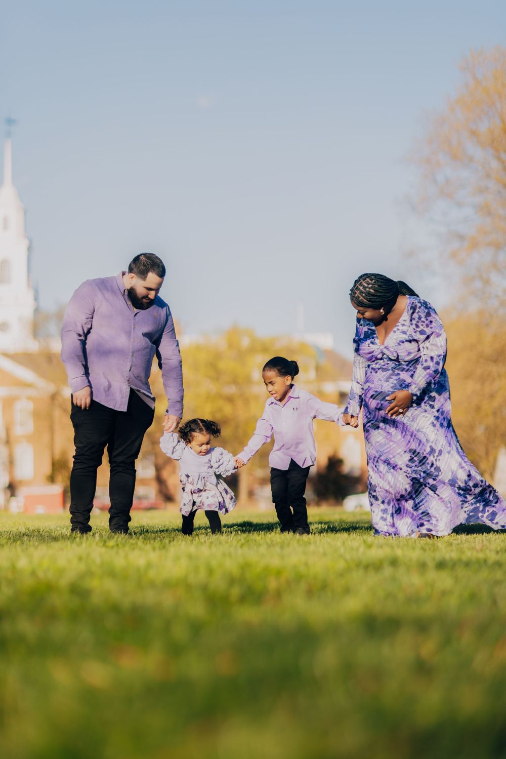 A family walks together on grass with a church steeple visible in the background.