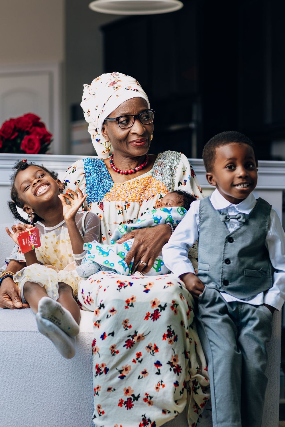 Woman in floral dress sharing joyful moment with two children on white sofa.