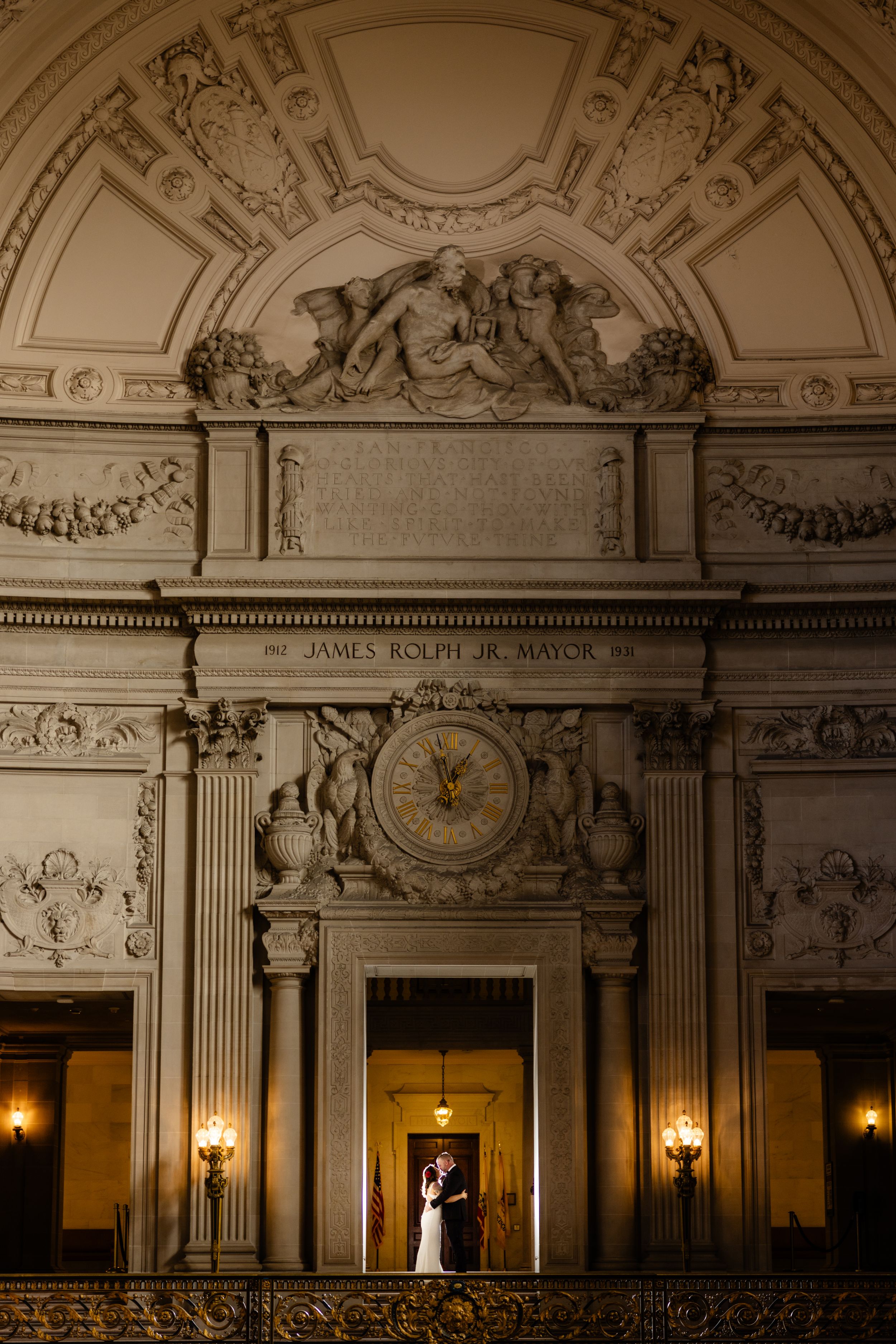 Silhouette of a couple framed in doorway beneath elaborate ceiling sculptures and wall sconces.