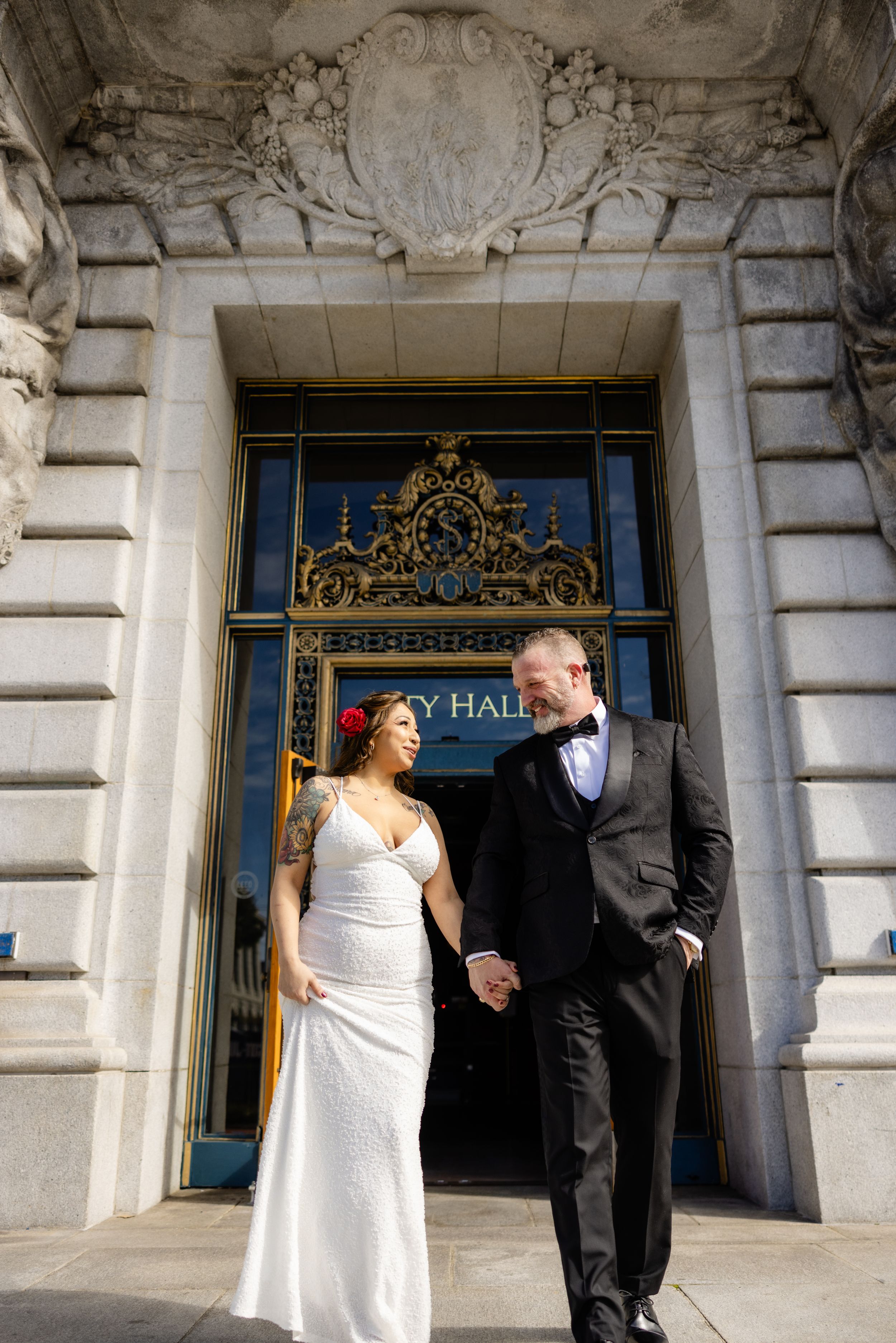 Wedding couple posing in front of ornate City Hall entrance with decorative gold details.