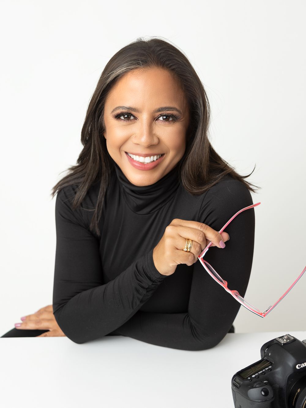 Professional headshot of person in black turtleneck with camera equipment on white background.