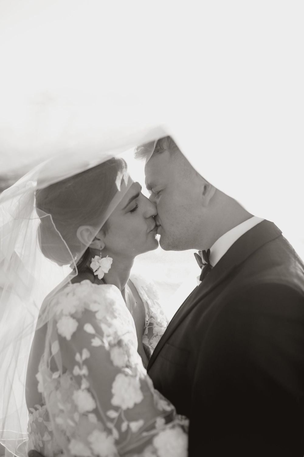 A romantic black and white wedding photo of a couple sharing a kiss under a delicate veil.