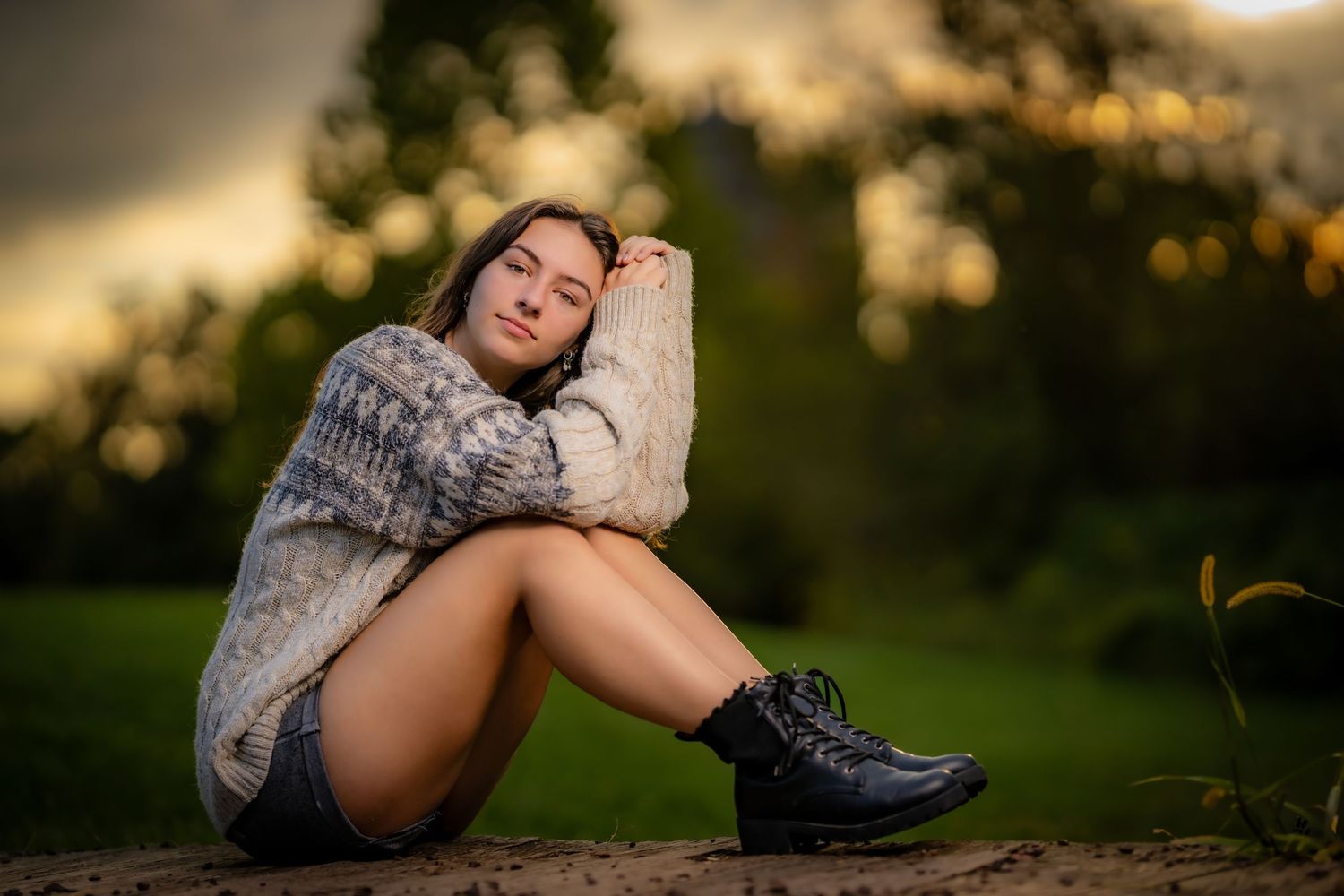 Person in sweater sits outdoors during golden hour with boots on.