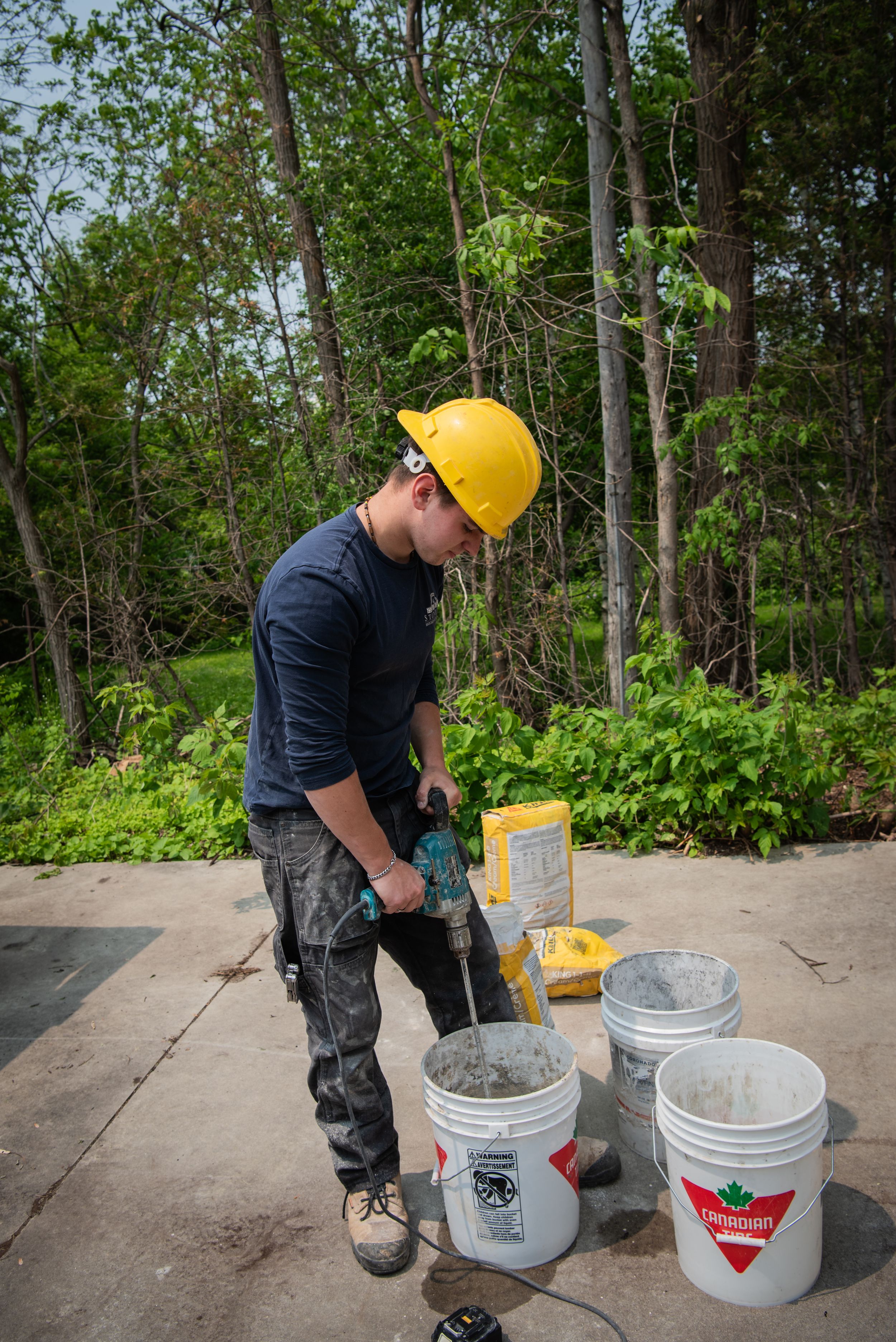 Worker in protective gear mixes construction materials in multiple white buckets outdoors.