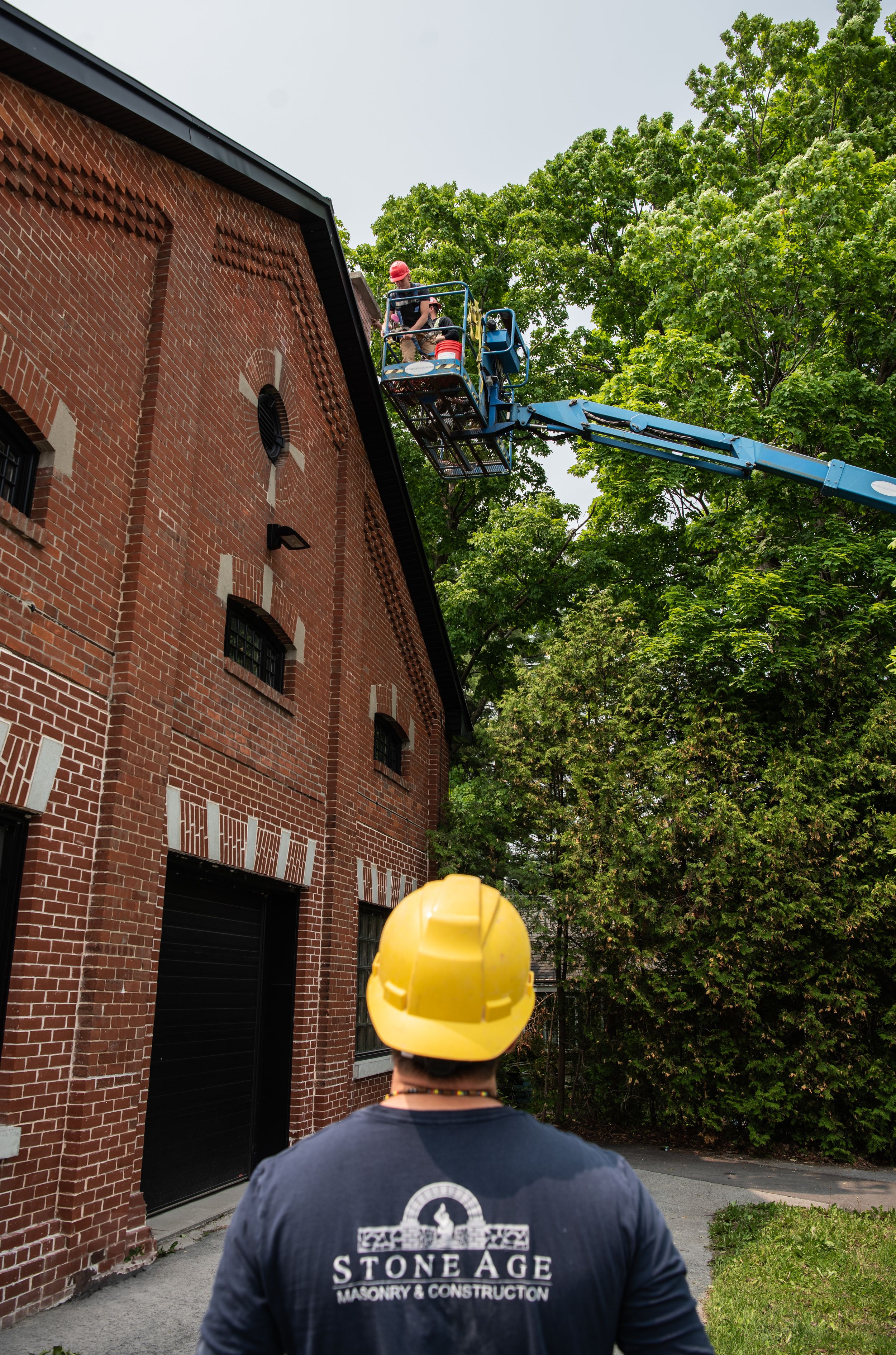 Construction worker in yellow hard hat inspects brick building exterior during maintenance work at historic site.
