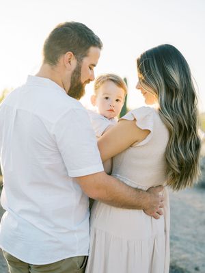A family in white and beige outfits shares tender moments together on a sunny beach during a photography session.
