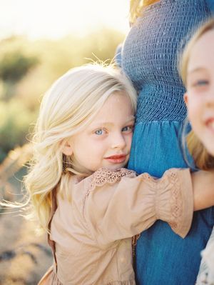 A child in a beige sweater hugs someone wearing blue denim during a warm sunset photoshoot.