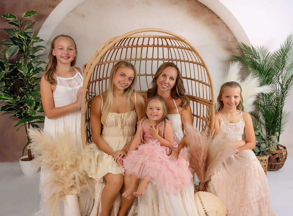 Bohemian styled indoor portrait with wicker egg chair, greenery, and soft natural lighting.