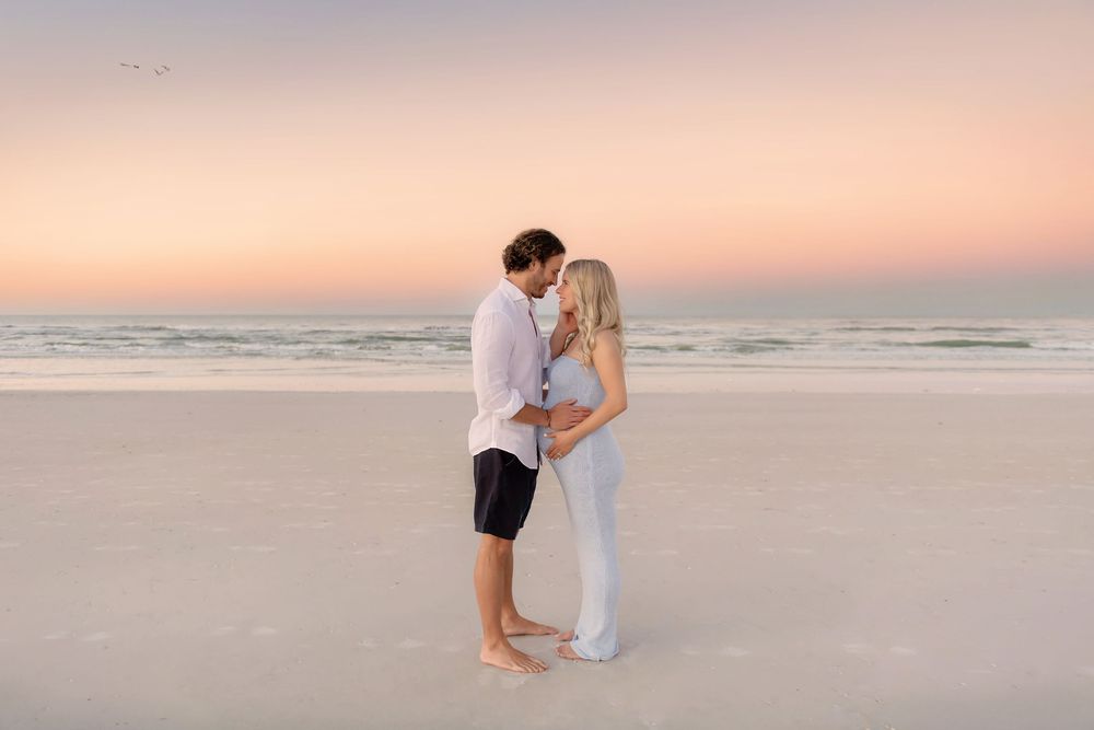 Romantic beach photoshoot during golden hour sunset with soft pink sky.
