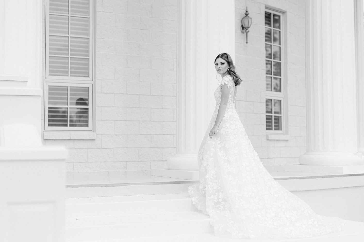 Black and white bridal portrait showing full length lace gown against white building.