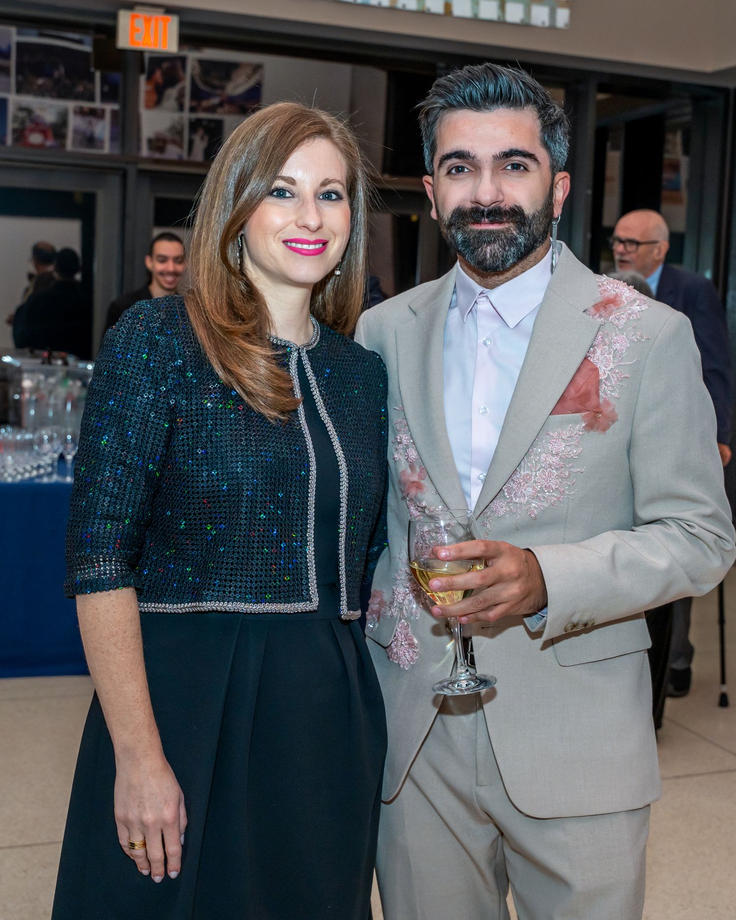 Elegant couple at formal event, woman in navy dress and man in embroidered beige suit.