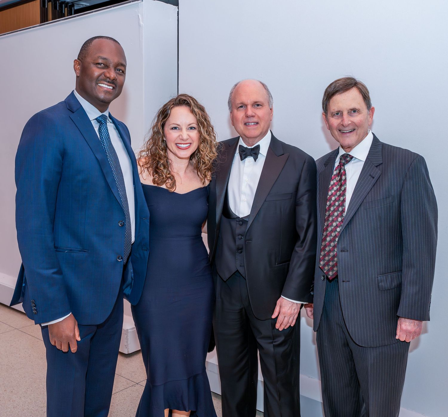 Four professionals in formal attire pose together at evening event.