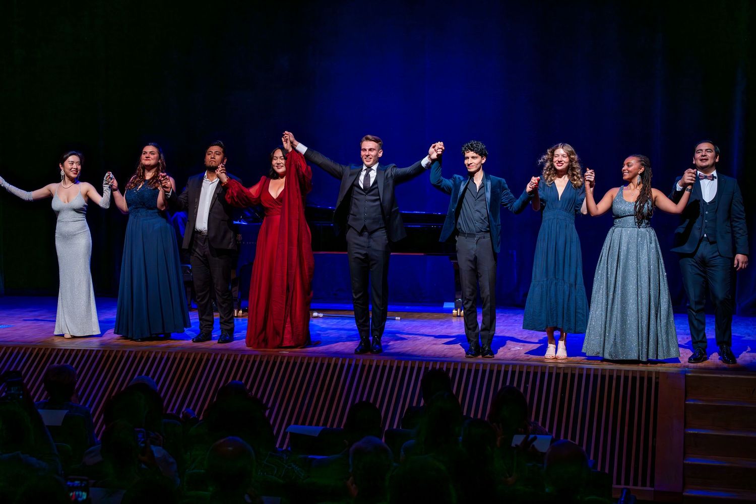 Group performance on stage with dramatic blue lighting and formal attire during theatrical production.