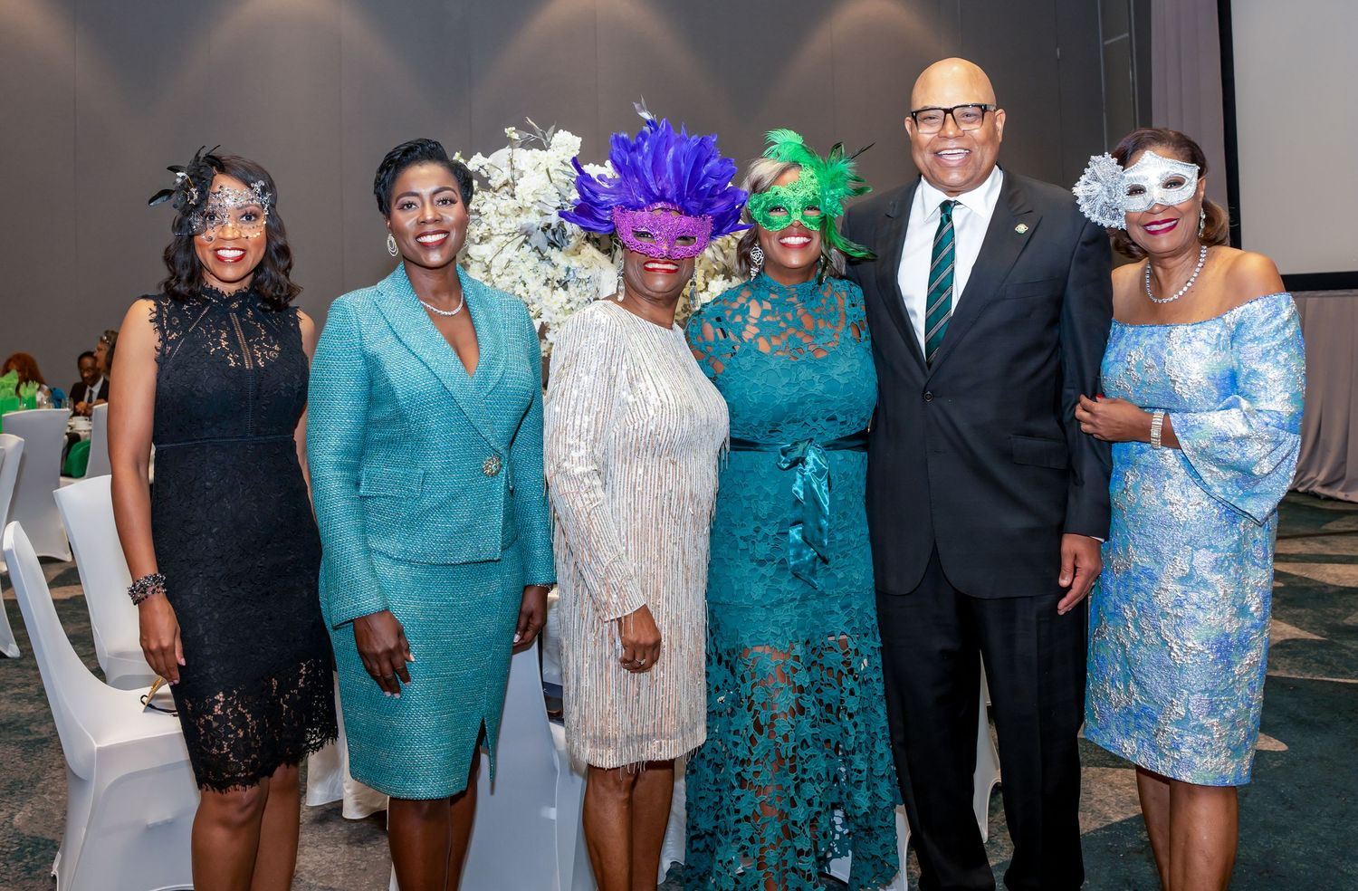 Event attendees in formal wear and masquerade masks posing together at social function.