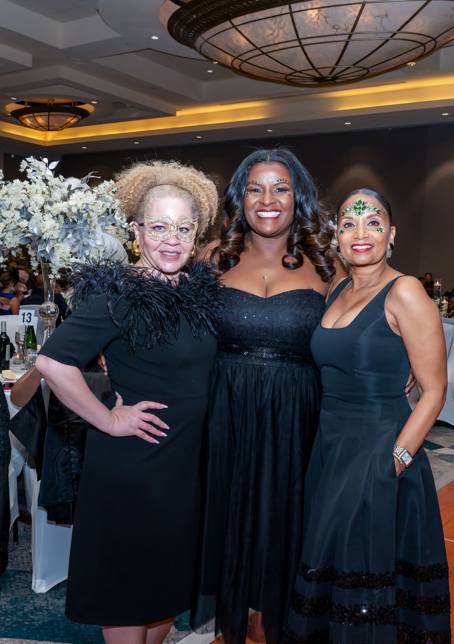 Women in coordinated black dresses posing together at a formal evening event.