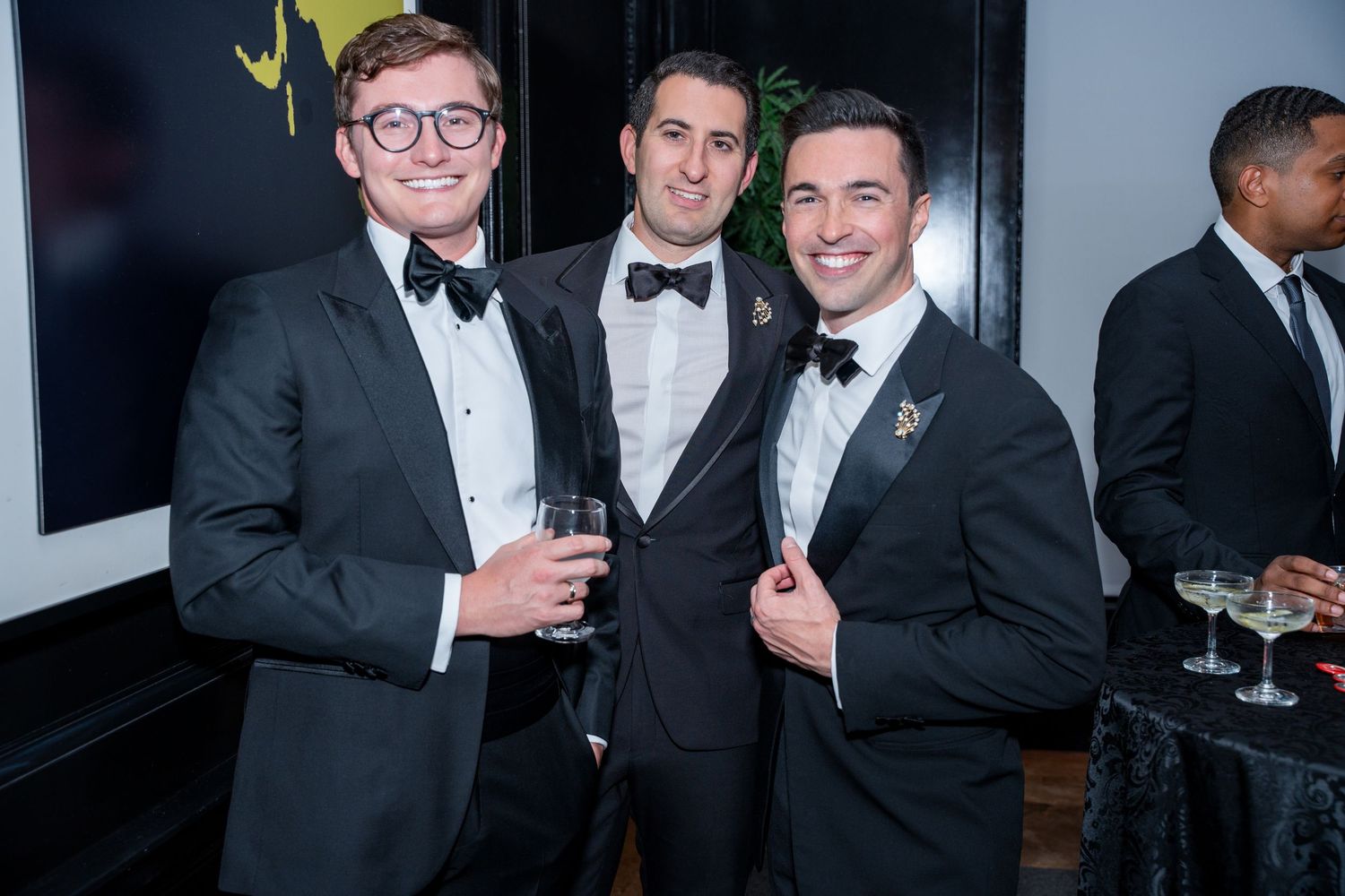 Three men in tuxedos pose together at a formal evening event.