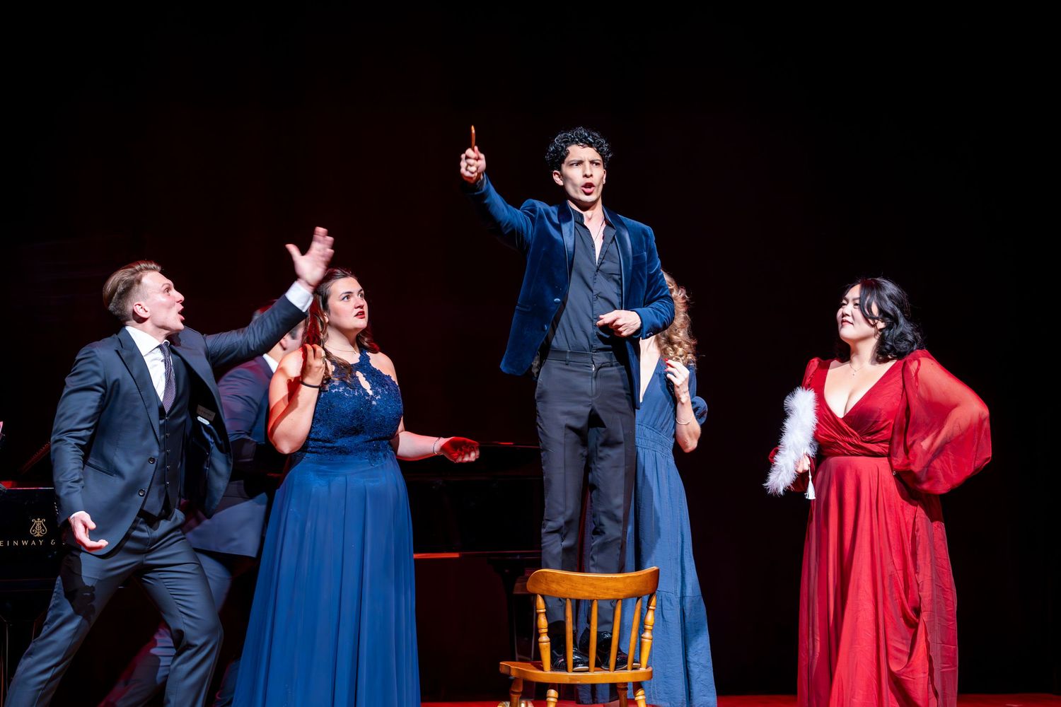 Performers in formal attire present an energetic stage performance with dramatic gestures.