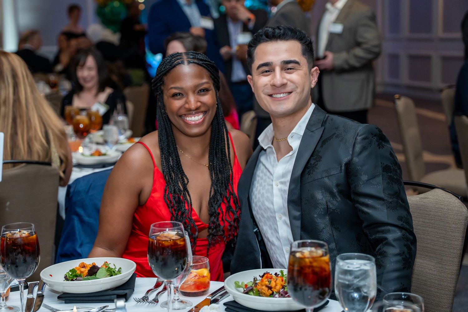 Guests enjoying dinner and drinks at formal event tables with plated meals.