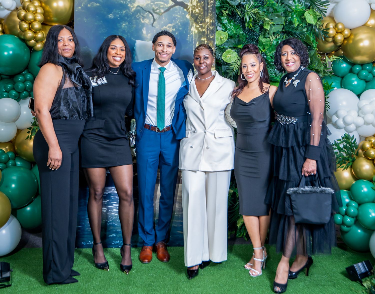 Group photo with gold and green balloon arch backdrop at formal celebration.