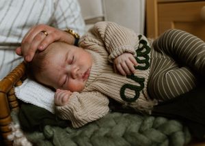 A peaceful newborn baby sleeps in a knit outfit on a soft green blanket during a newborn photography session.