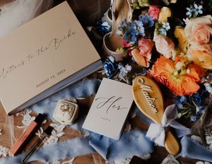 Flat lay of wedding details including Letters to the Bride journal, ring box, and colorful florals.
