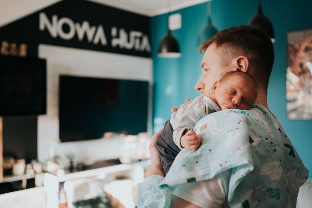 tata trzyma na ramieniu noworodka, w tle salon - fotograf Kraków