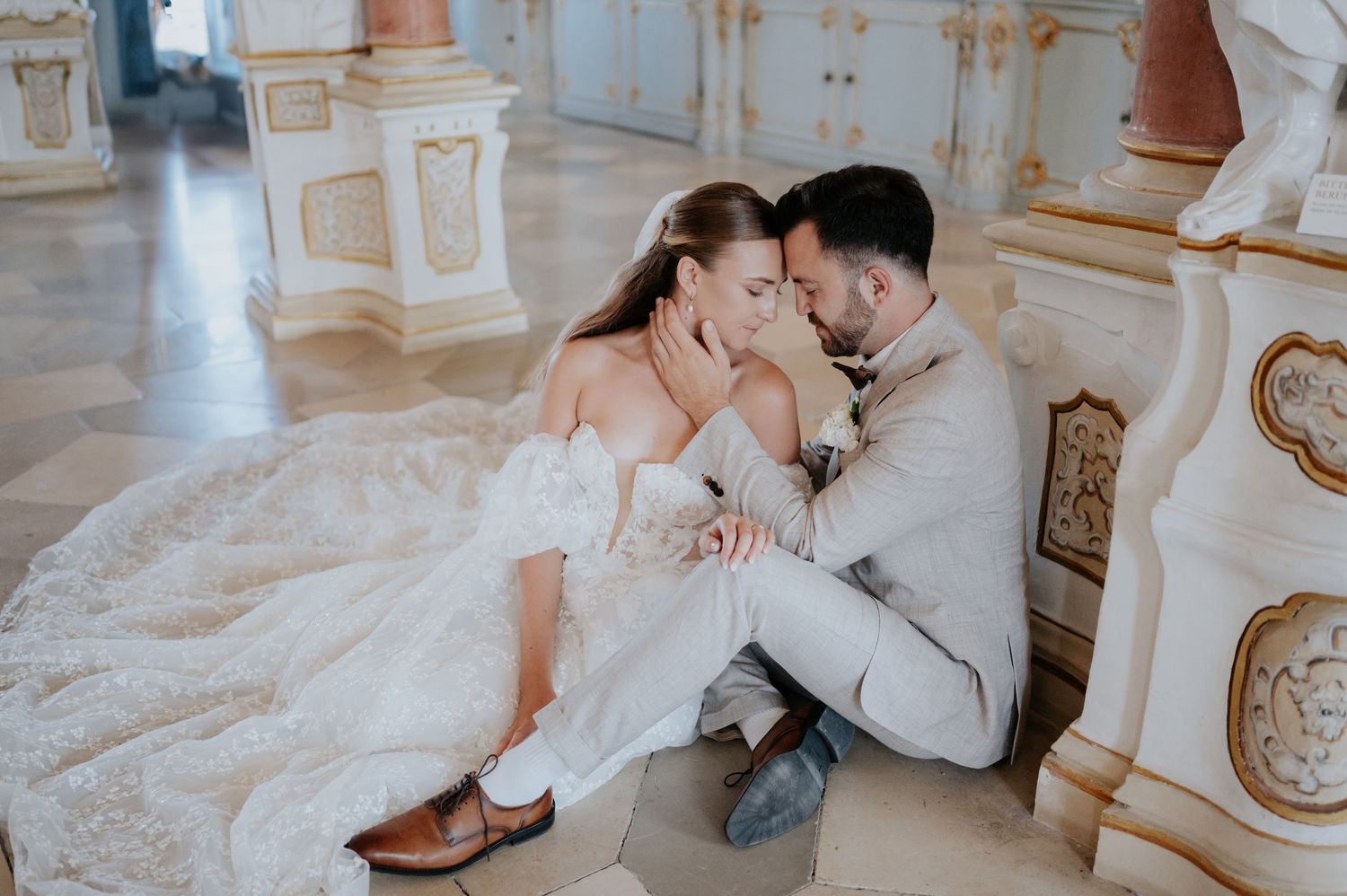 Ein romantisches Hochzeitspaar teilt einen intimen Moment auf einem kunstvoll verzierten weißen Marmorboden in einer eleganten Location.