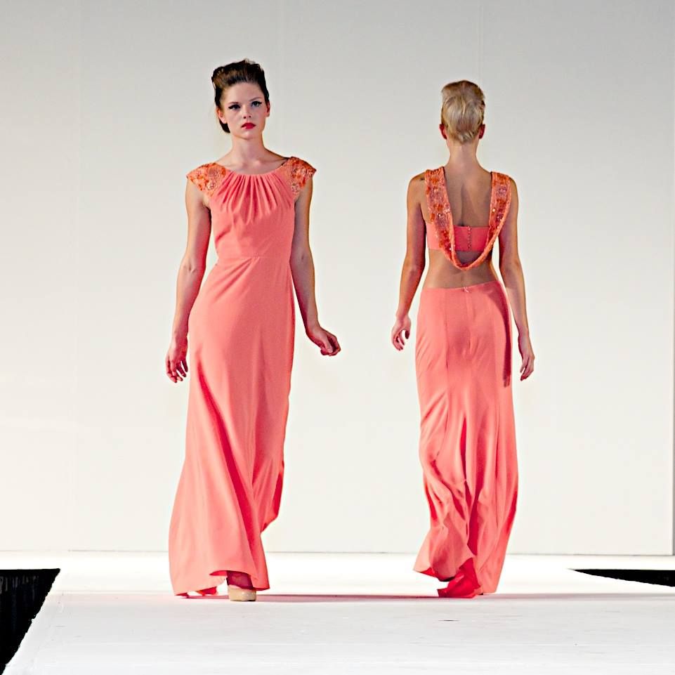 Models walk the runway in flowing coral evening gowns with delicate lace details and open back designs.